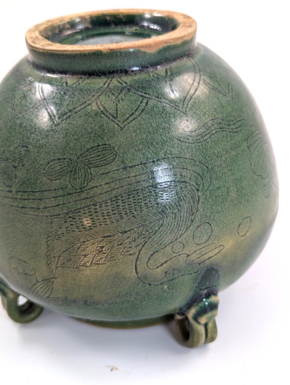 A rounded olive green celadon ceramic jar with four loop handles along the rim, featuring crackle glaze and incised line drawings of ducks and lotus plants. View IX