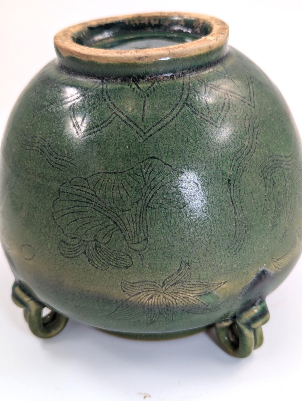 A rounded olive green celadon ceramic jar with four loop handles along the rim, featuring crackle glaze and incised line drawings of ducks and lotus plants. View X