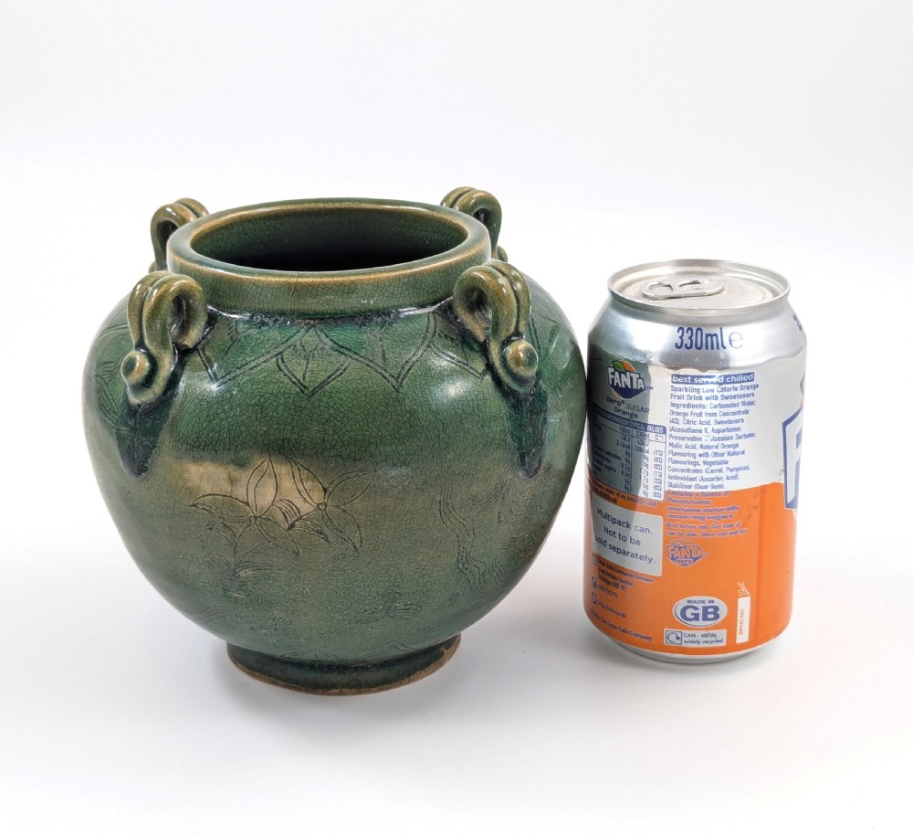 A rounded olive green celadon ceramic jar with four loop handles along the rim, featuring crackle glaze and incised line drawings of ducks and lotus plants. View XII