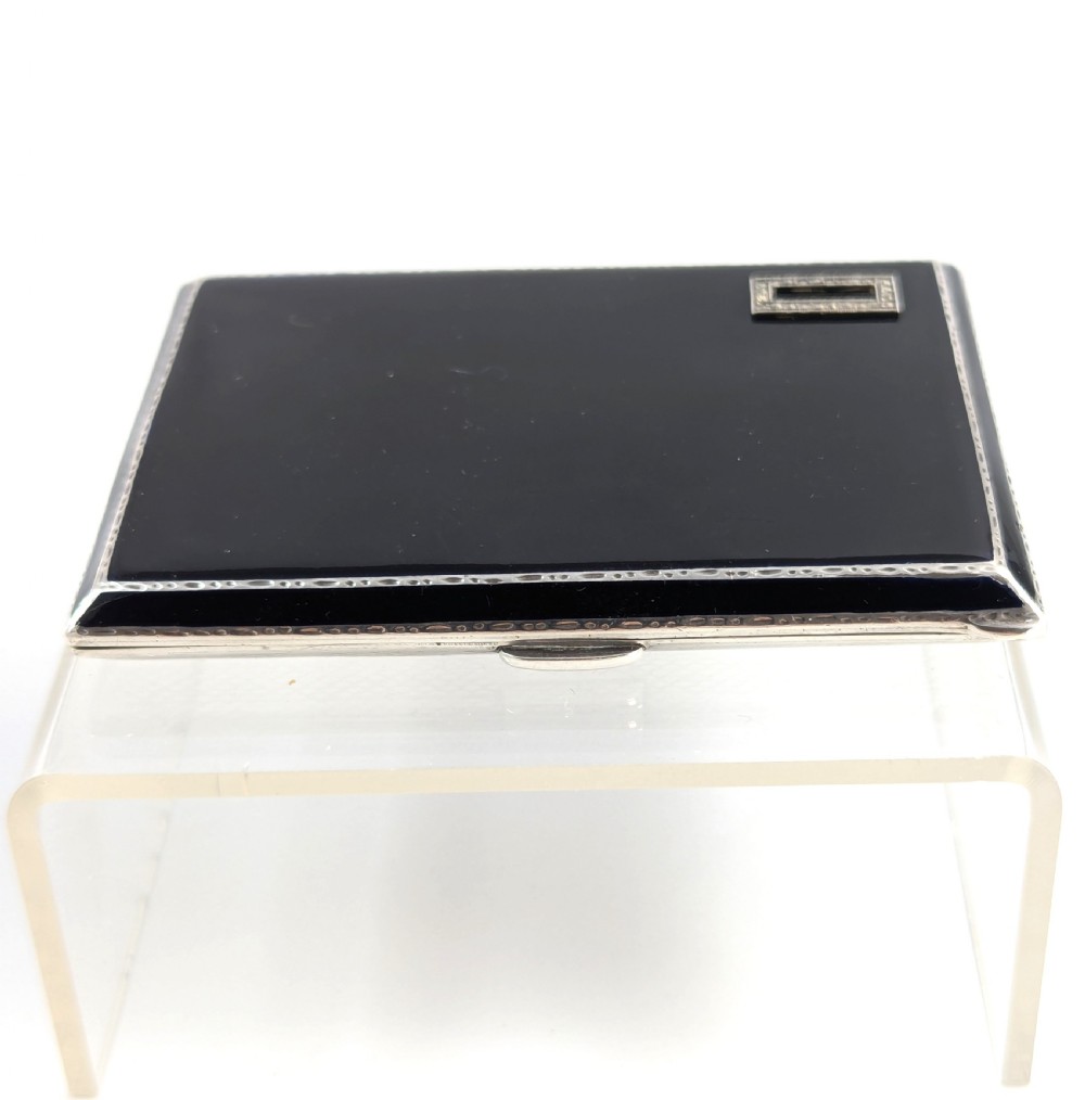 An Art Deco rectangular sterling silver cigarette case featuring a polished black enamel cover with a marcasite-inset rectangular corner detail and a beige suede pouch. View VII