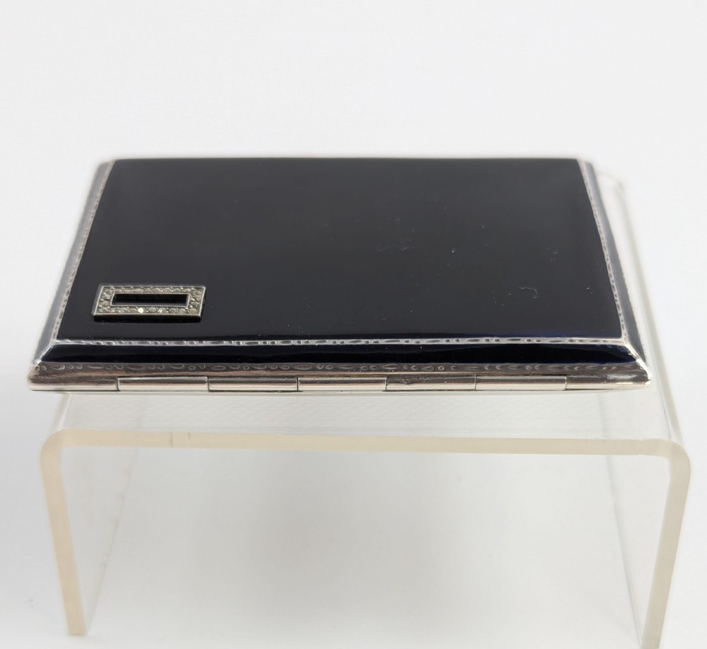 An Art Deco rectangular sterling silver cigarette case featuring a polished black enamel cover with a marcasite-inset rectangular corner detail and a beige suede pouch. View IX