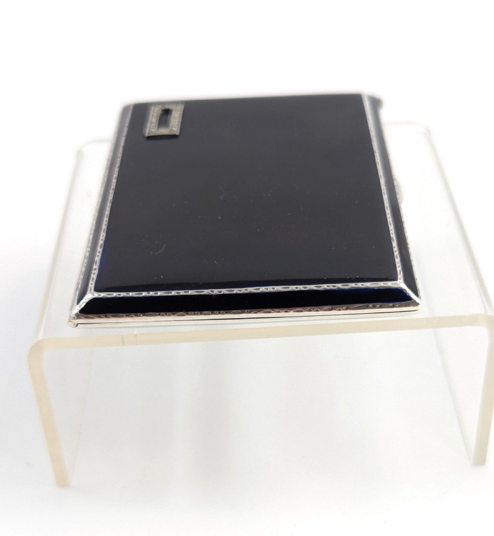 An Art Deco rectangular sterling silver cigarette case featuring a polished black enamel cover with a marcasite-inset rectangular corner detail and a beige suede pouch. View X