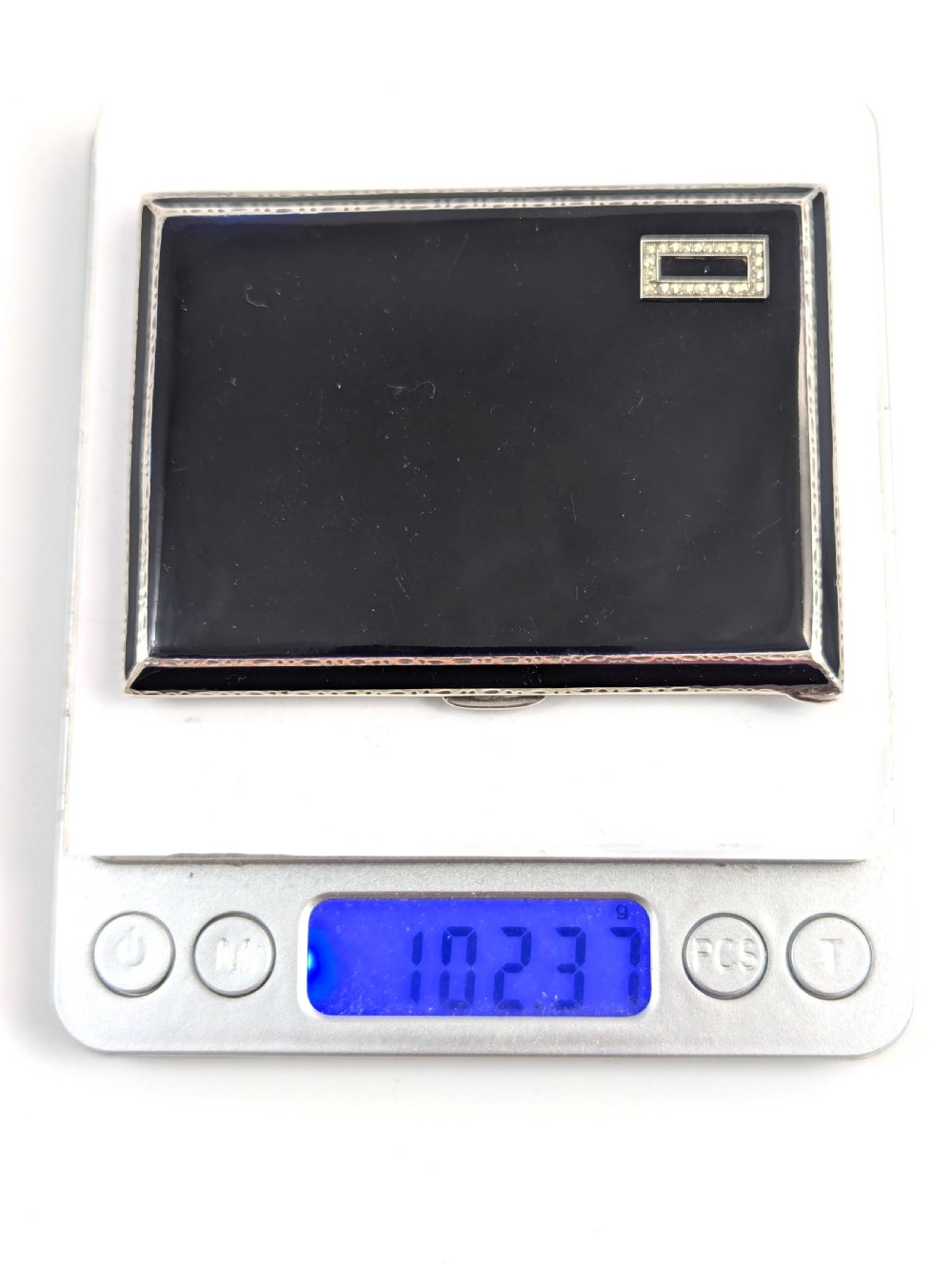 An Art Deco rectangular sterling silver cigarette case featuring a polished black enamel cover with a marcasite-inset rectangular corner detail and a beige suede pouch. View XI
