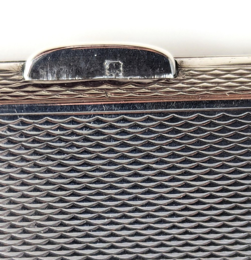 An Art Deco rectangular sterling silver cigarette case featuring a polished black enamel cover with a marcasite-inset rectangular corner detail and a beige suede pouch. View XII