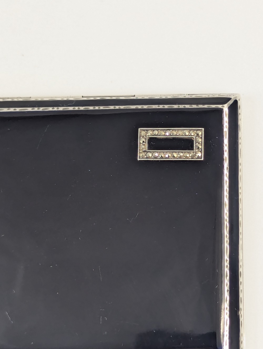 An Art Deco rectangular sterling silver cigarette case featuring a polished black enamel cover with a marcasite-inset rectangular corner detail and a beige suede pouch. View XIV