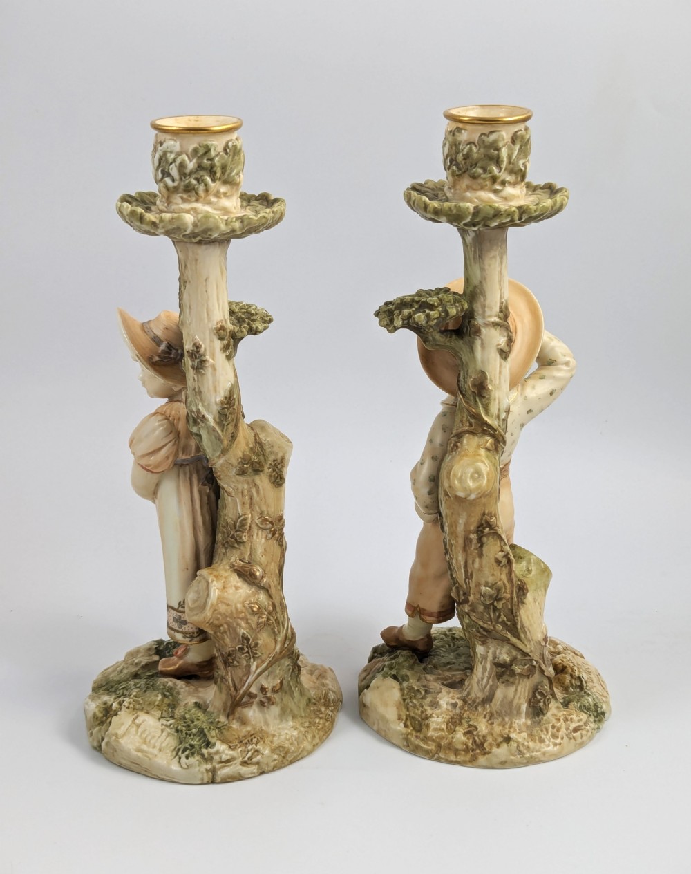 A pair of Victorian Royal Worcester porcelain candlesticks featuring a young boy and girl standing before tree trunk columns topped with leafy candle sconces. View III