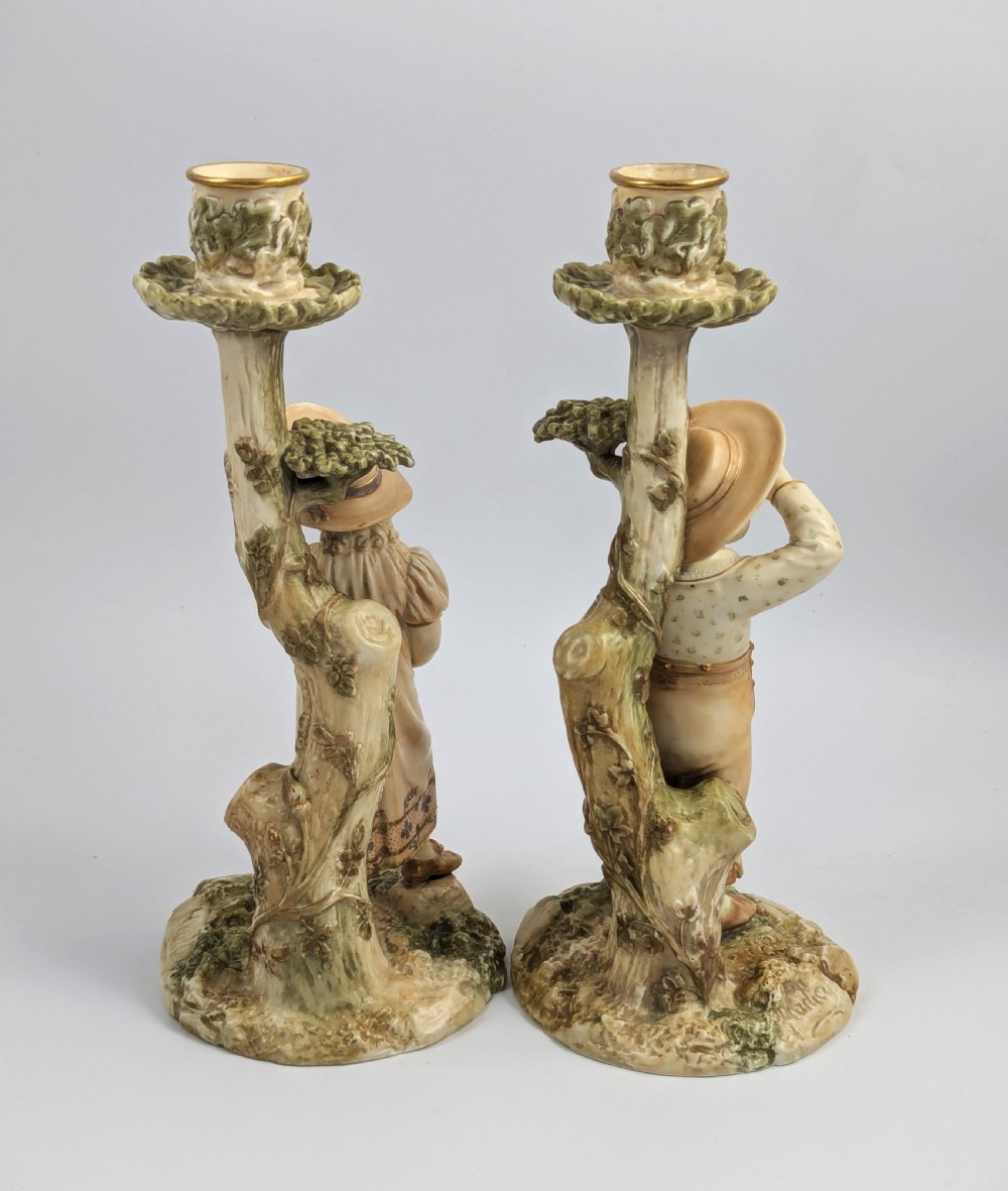 A pair of Victorian Royal Worcester porcelain candlesticks featuring a young boy and girl standing before tree trunk columns topped with leafy candle sconces. View IV