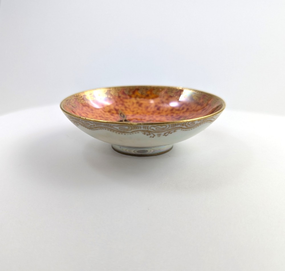 A small shallow ceramic bowl featuring a mottled orange iridescent lustre interior with gilt edging and a light pearlescent exterior. View IV