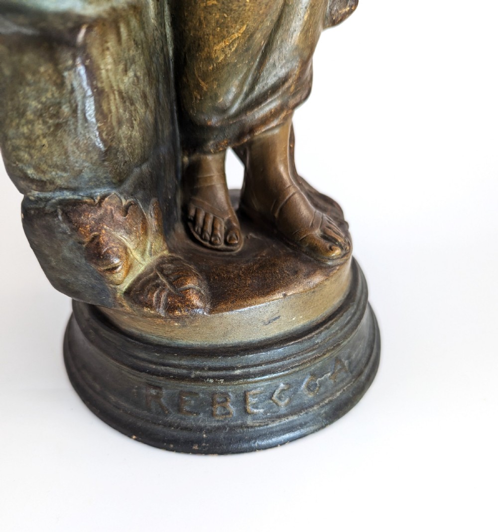 An Art Nouveau earthenware figurine depicting a draped female figure resting against a water pitcher on a stone-effect pillar. View IX