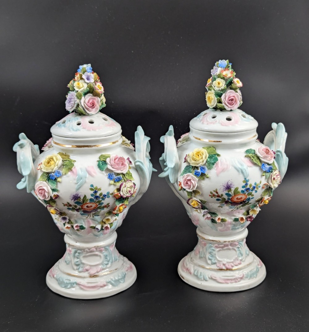 A pair of antique Sitzendorf hard-paste white porcelain potpourri vases decorated with encrusted hand-moulded flowers, scrolling handles, pierced lids, and painted floral sprays. View V