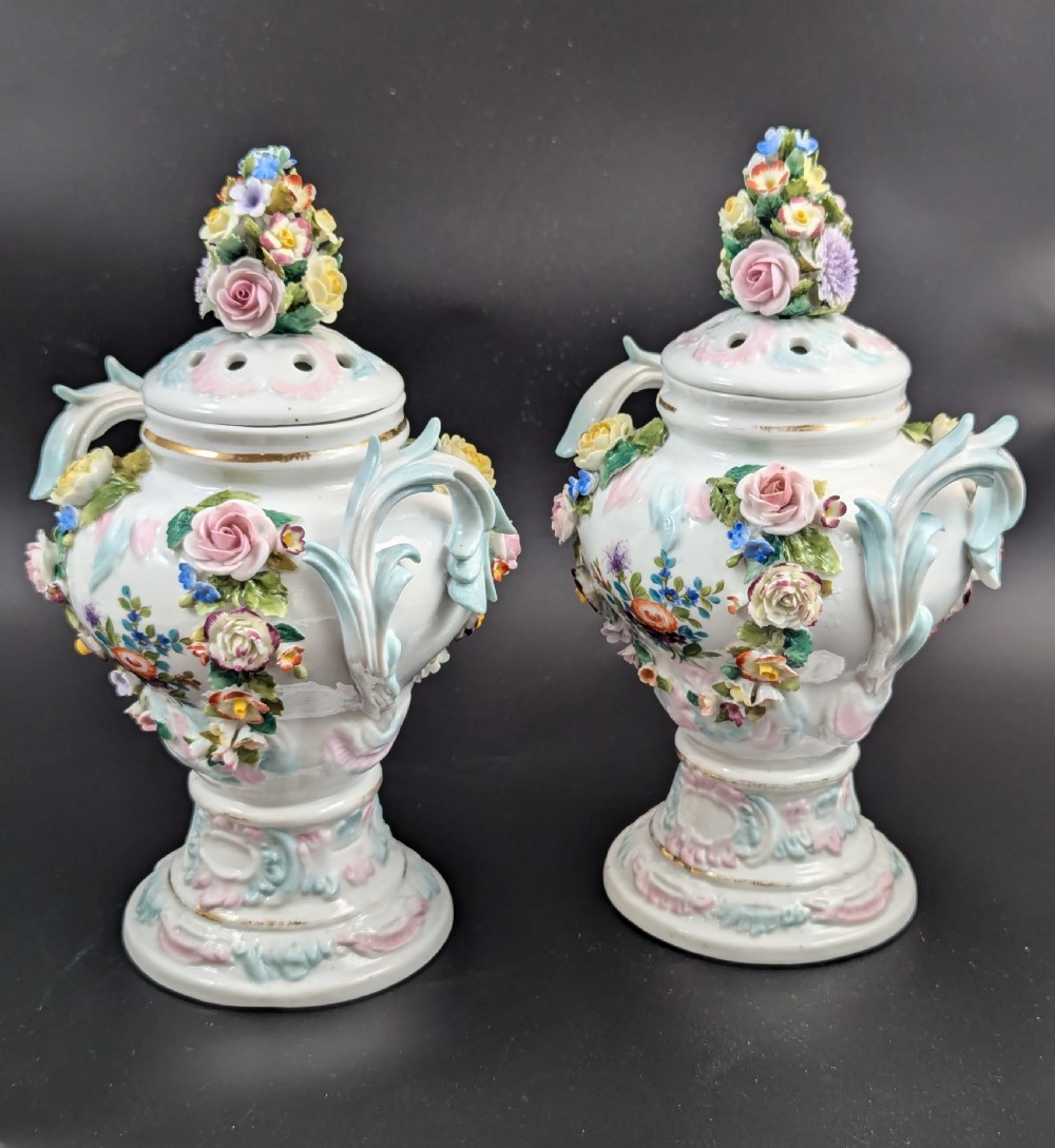 A pair of antique Sitzendorf hard-paste white porcelain potpourri vases decorated with encrusted hand-moulded flowers, scrolling handles, pierced lids, and painted floral sprays. View VI