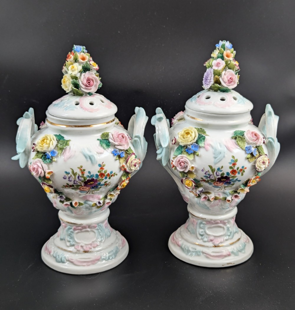 A pair of antique Sitzendorf hard-paste white porcelain potpourri vases decorated with encrusted hand-moulded flowers, scrolling handles, pierced lids, and painted floral sprays. View IX