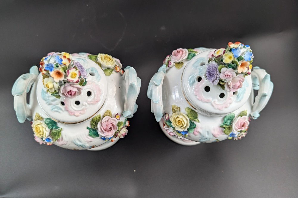 A pair of antique Sitzendorf hard-paste white porcelain potpourri vases decorated with encrusted hand-moulded flowers, scrolling handles, pierced lids, and painted floral sprays. View X