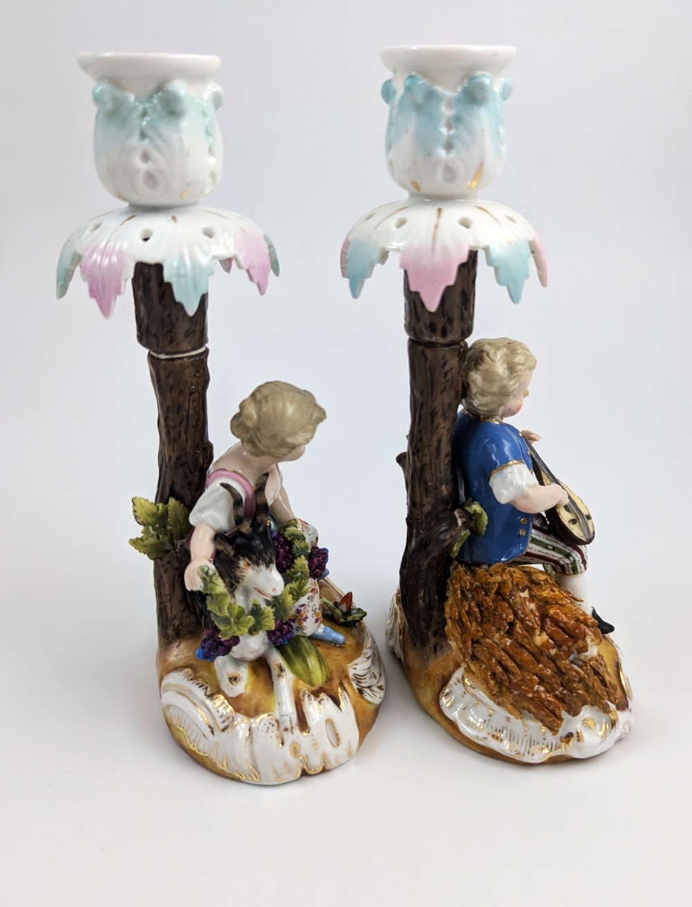 A pair of hand-painted German Sitzendorf porcelain figural candlesticks featuring a shepherdess and a lute player seated beside tree trunks supporting leafy sconces. View IV