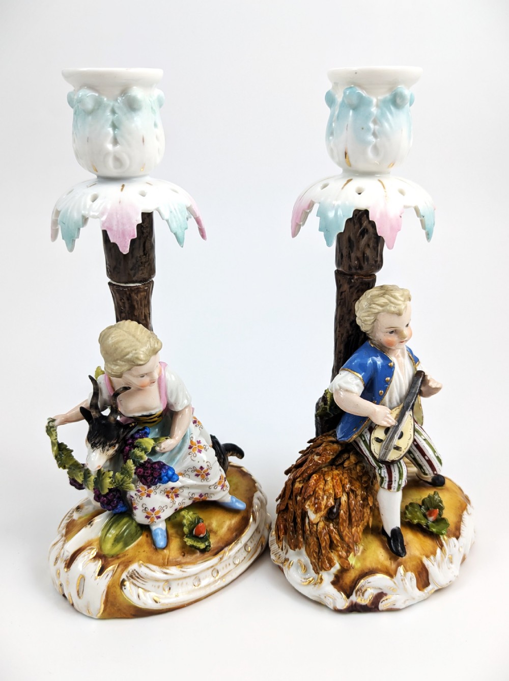A pair of hand-painted German Sitzendorf porcelain figural candlesticks featuring a shepherdess and a lute player seated beside tree trunks supporting leafy sconces. View V