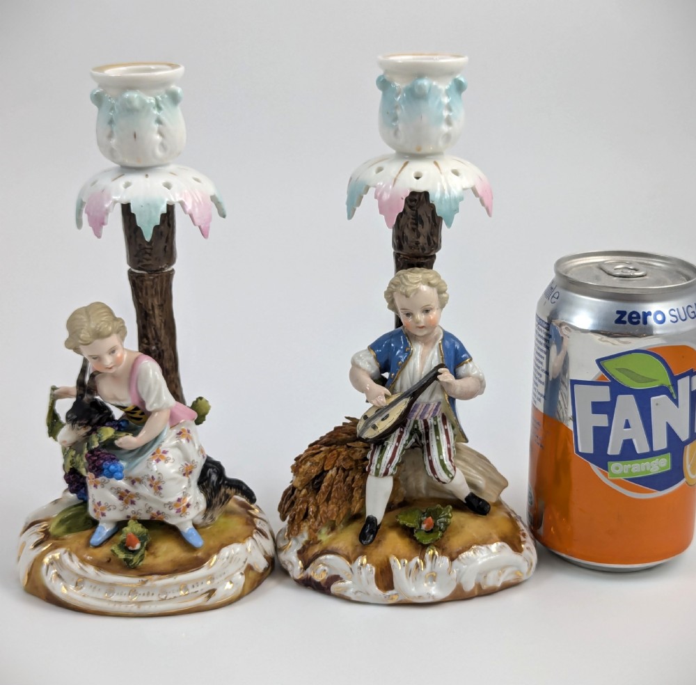 A pair of hand-painted German Sitzendorf porcelain figural candlesticks featuring a shepherdess and a lute player seated beside tree trunks supporting leafy sconces. View VIII