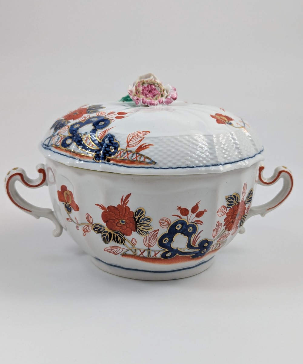An antique white porcelain lidded broth cup decorated with hand-painted red and blue floral motifs, featuring twin scroll handles and a sculpted floral lid finial. View IV