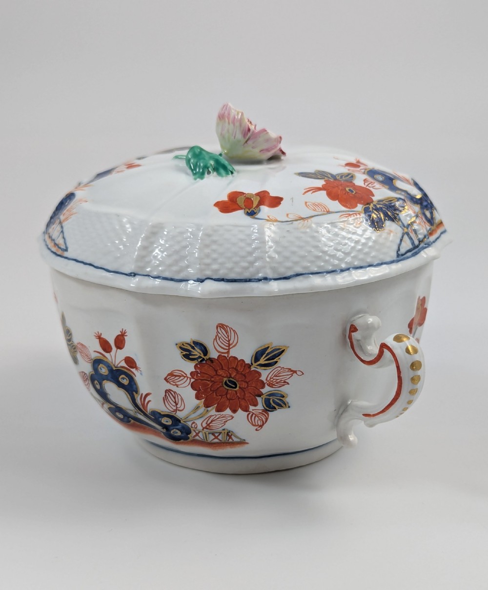 An antique white porcelain lidded broth cup decorated with hand-painted red and blue floral motifs, featuring twin scroll handles and a sculpted floral lid finial. View VI