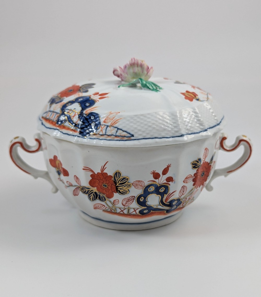 An antique white porcelain lidded broth cup decorated with hand-painted red and blue floral motifs, featuring twin scroll handles and a sculpted floral lid finial. View VII