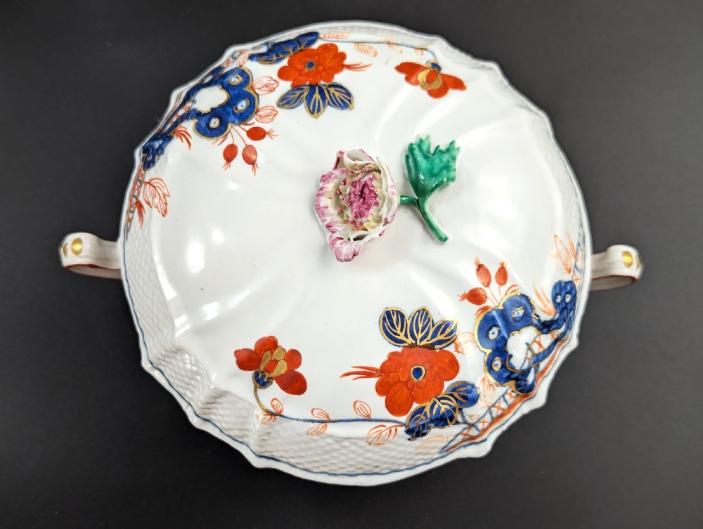 An antique white porcelain lidded broth cup decorated with hand-painted red and blue floral motifs, featuring twin scroll handles and a sculpted floral lid finial. View VIII