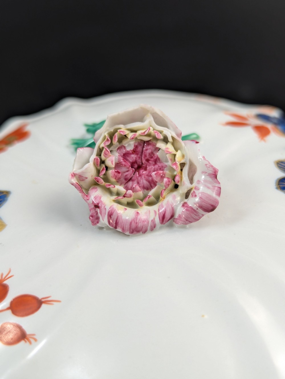 An antique white porcelain lidded broth cup decorated with hand-painted red and blue floral motifs, featuring twin scroll handles and a sculpted floral lid finial. View IX