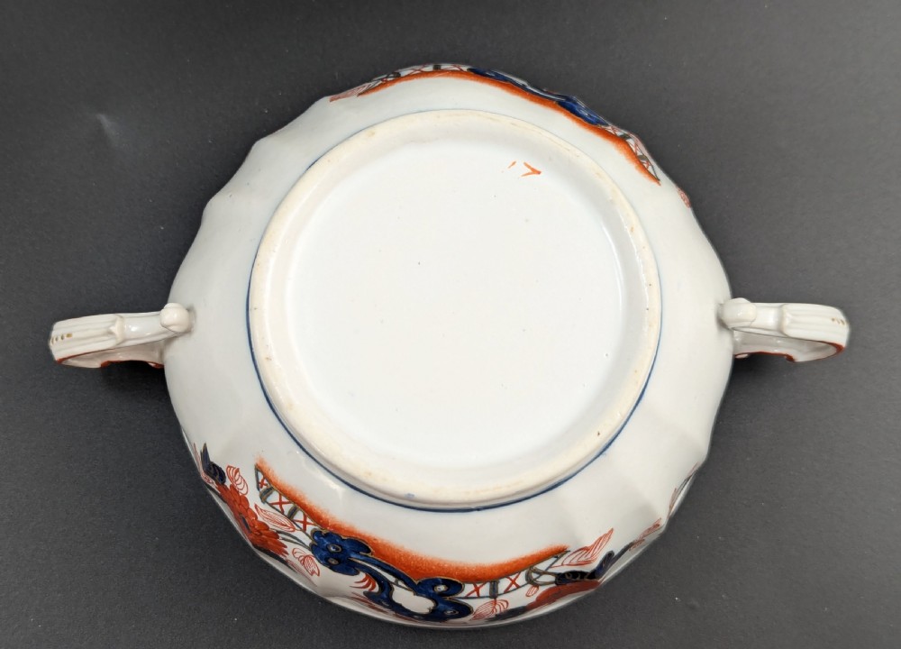 An antique white porcelain lidded broth cup decorated with hand-painted red and blue floral motifs, featuring twin scroll handles and a sculpted floral lid finial. View XI