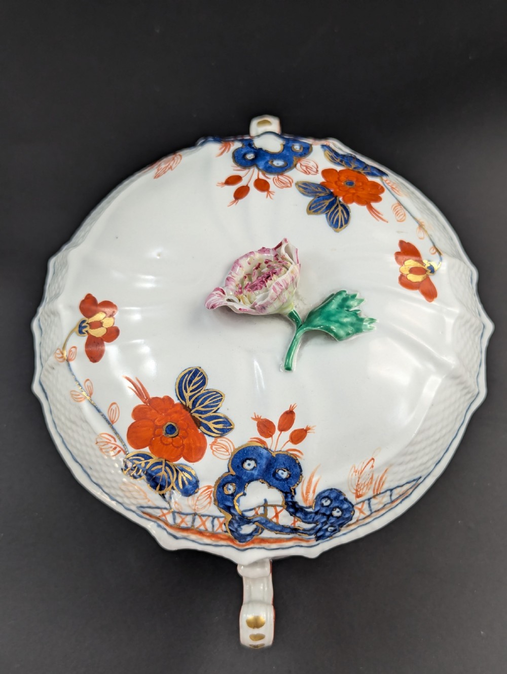 An antique white porcelain lidded broth cup decorated with hand-painted red and blue floral motifs, featuring twin scroll handles and a sculpted floral lid finial. View XIII