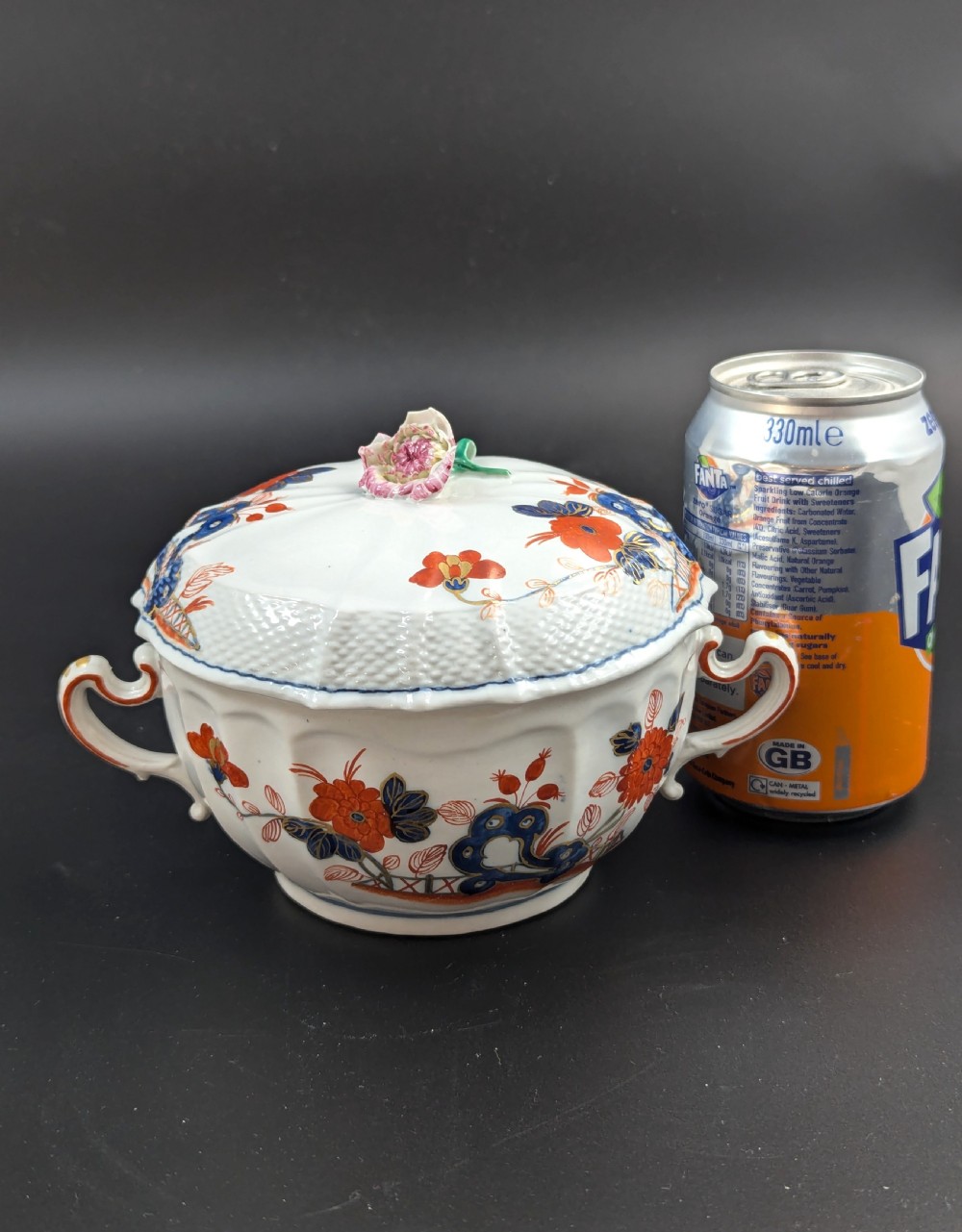 An antique white porcelain lidded broth cup decorated with hand-painted red and blue floral motifs, featuring twin scroll handles and a sculpted floral lid finial. View XIV