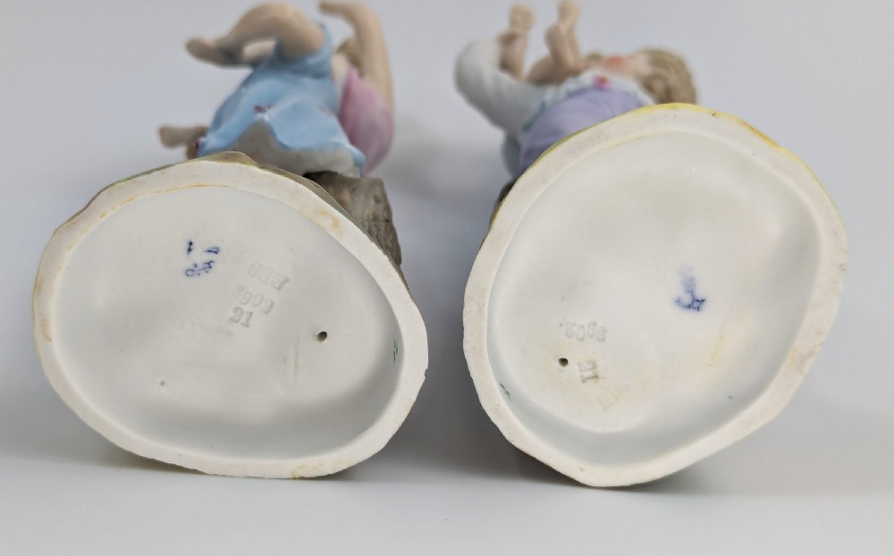 A pair of hand-painted German porcelain figurines depicting a boy and a girl carrying younger children piggyback style on tree stump bases. View VI