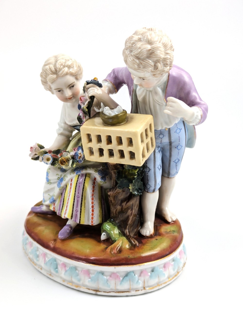 A nineteenth-century Meissen-style hand-painted porcelain figural group depicting two children with floral garlands beside a birdcage on a circular moulded base. View II