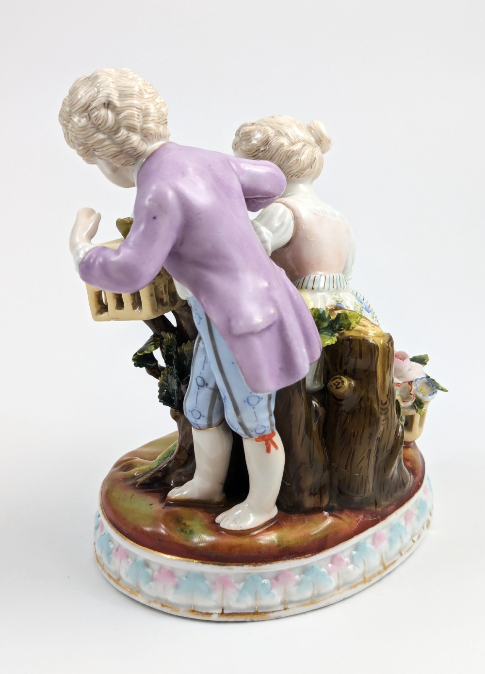 A nineteenth-century Meissen-style hand-painted porcelain figural group depicting two children with floral garlands beside a birdcage on a circular moulded base. View III