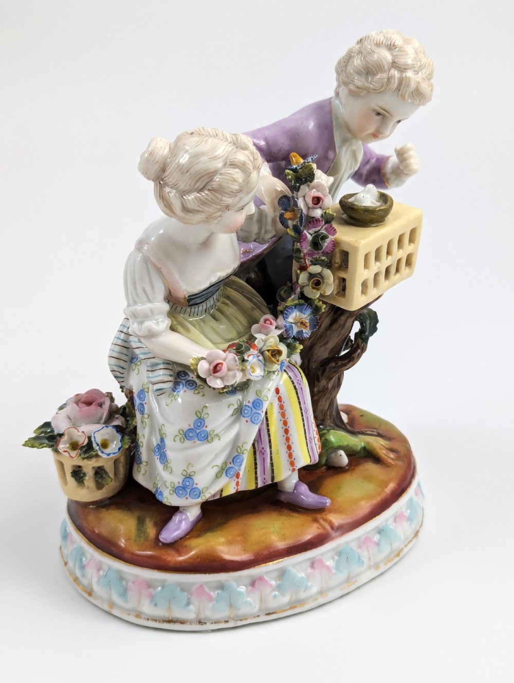 A nineteenth-century Meissen-style hand-painted porcelain figural group depicting two children with floral garlands beside a birdcage on a circular moulded base. View VI