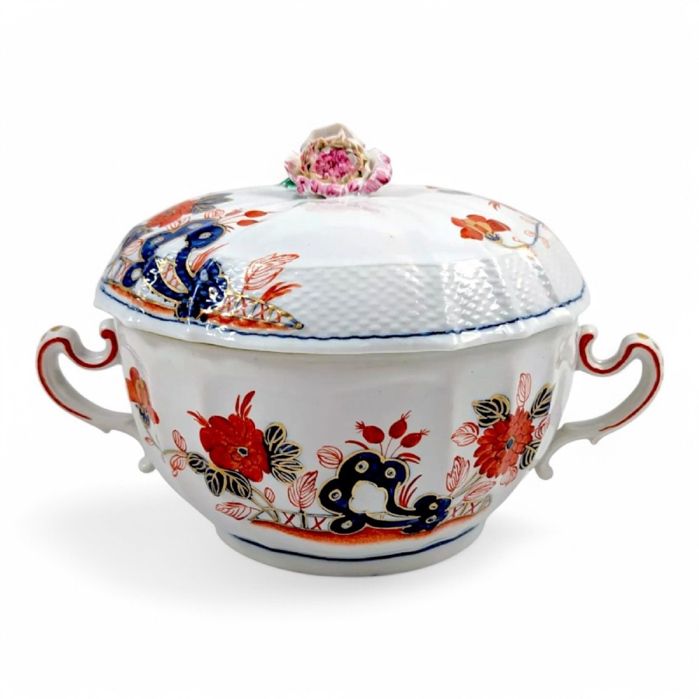 An antique white porcelain lidded broth cup decorated with hand-painted red and blue floral motifs, featuring twin scroll handles and a sculpted floral lid finial.