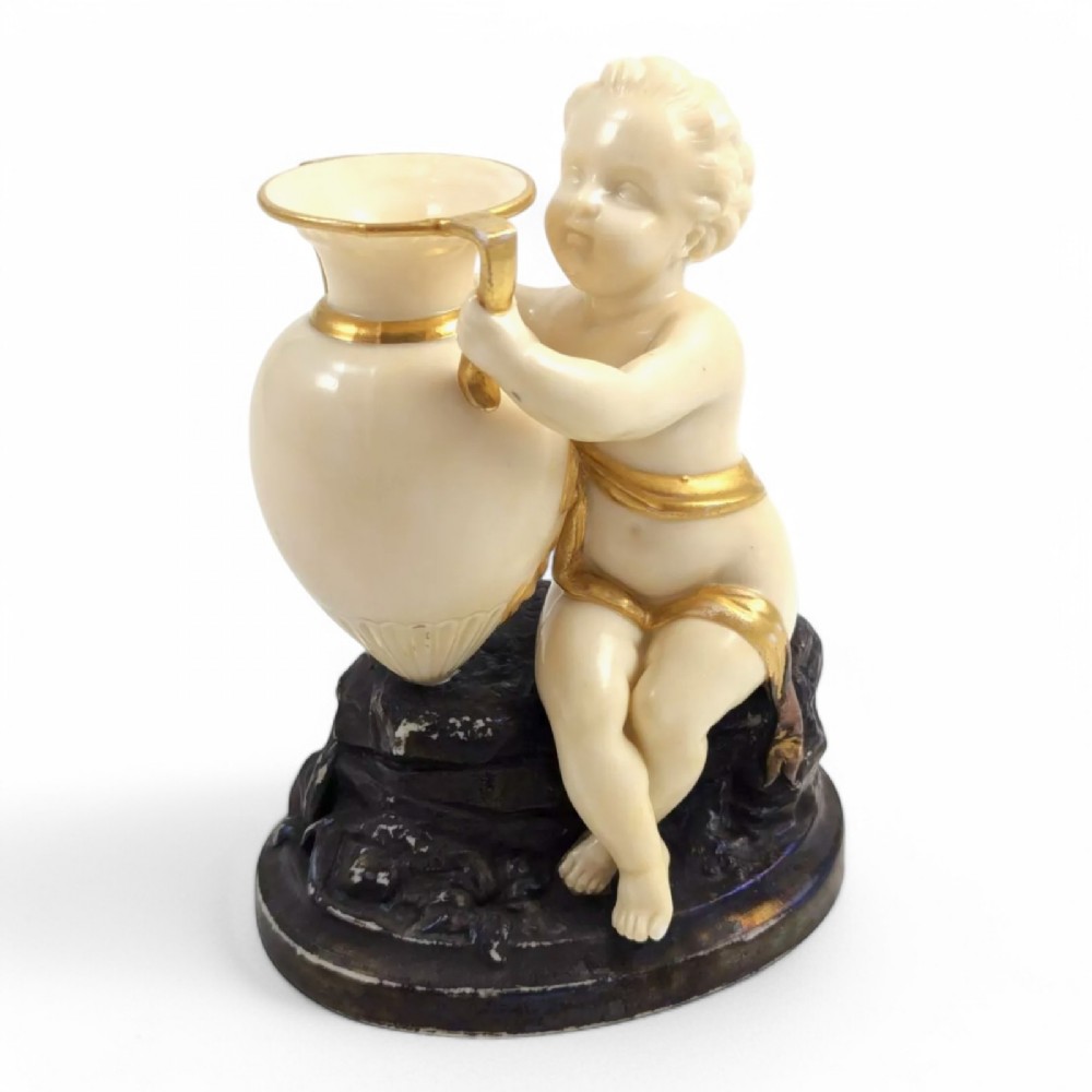 An ivory-coloured porcelain figurine depicting a small child seated beside a gilded amphora vessel on a dark base.