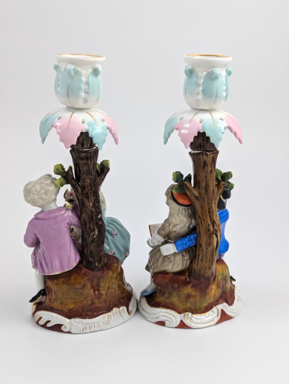A pair of hand-painted porcelain figural candlesticks depicting eighteenth-century styled children beside floral tree columns. View III