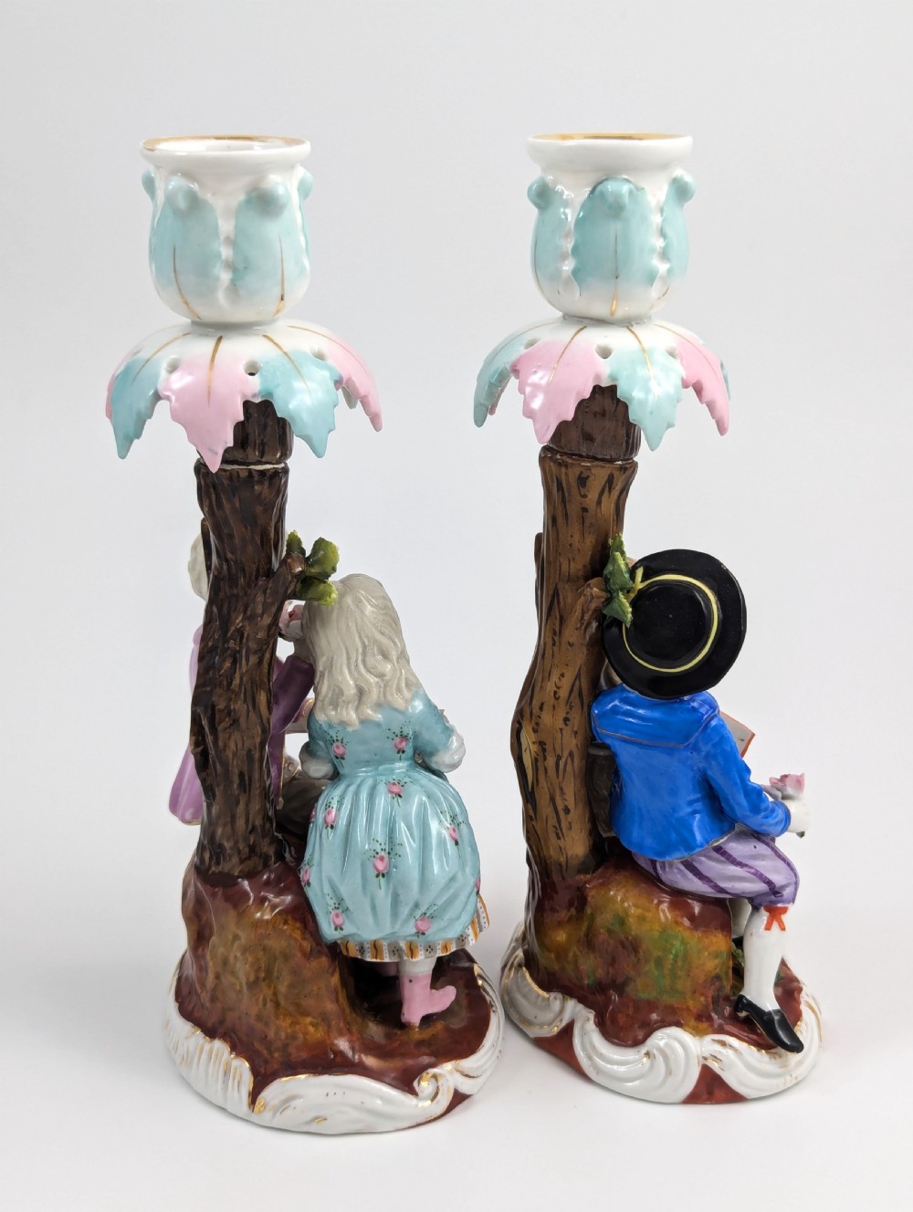 A pair of hand-painted porcelain figural candlesticks depicting eighteenth-century styled children beside floral tree columns. View IV