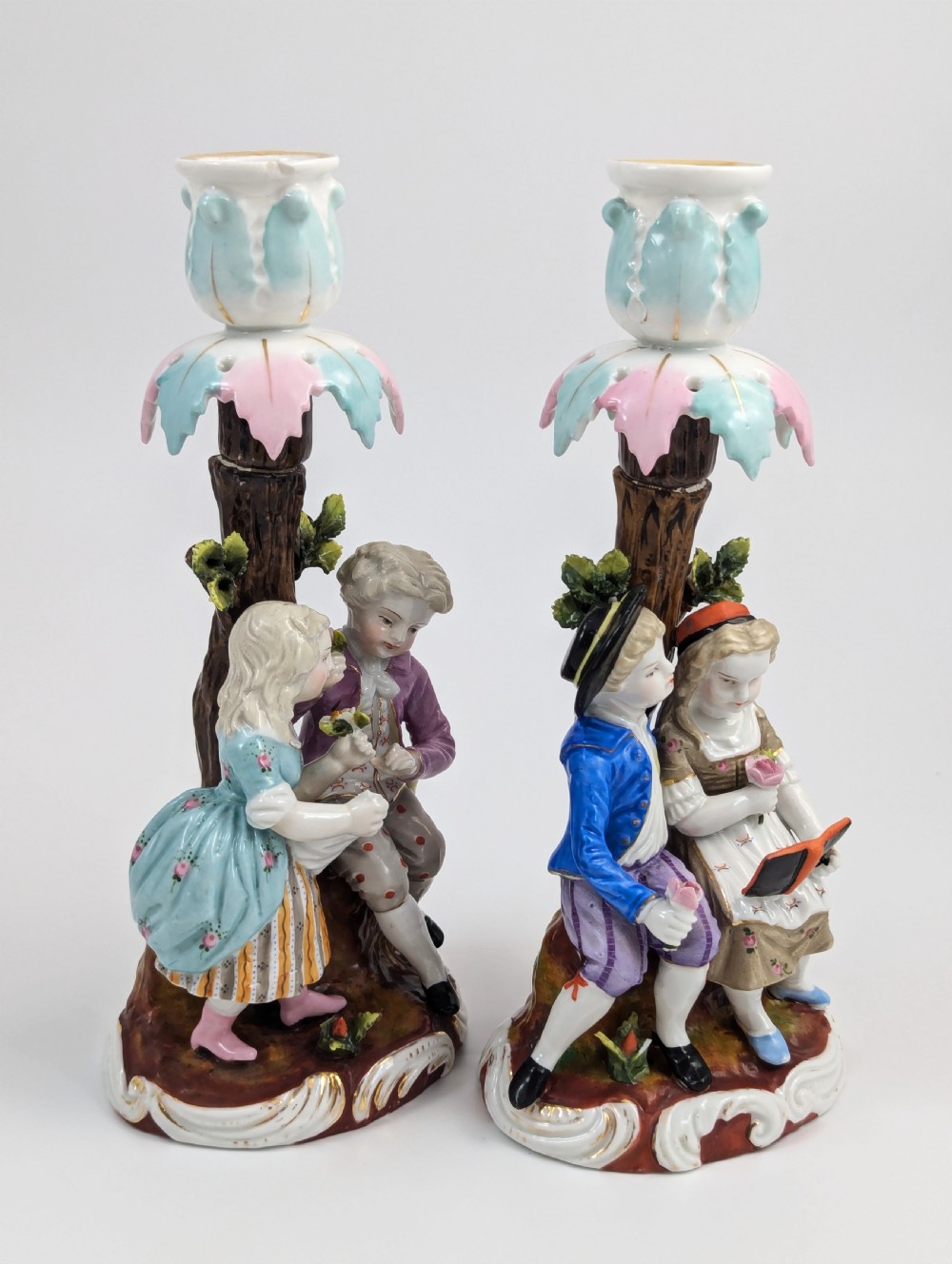 A pair of hand-painted porcelain figural candlesticks depicting eighteenth-century styled children beside floral tree columns. View V