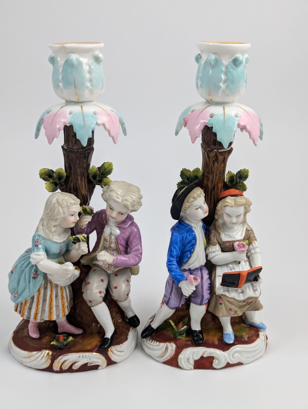 A pair of hand-painted porcelain figural candlesticks depicting eighteenth-century styled children beside floral tree columns. View VI
