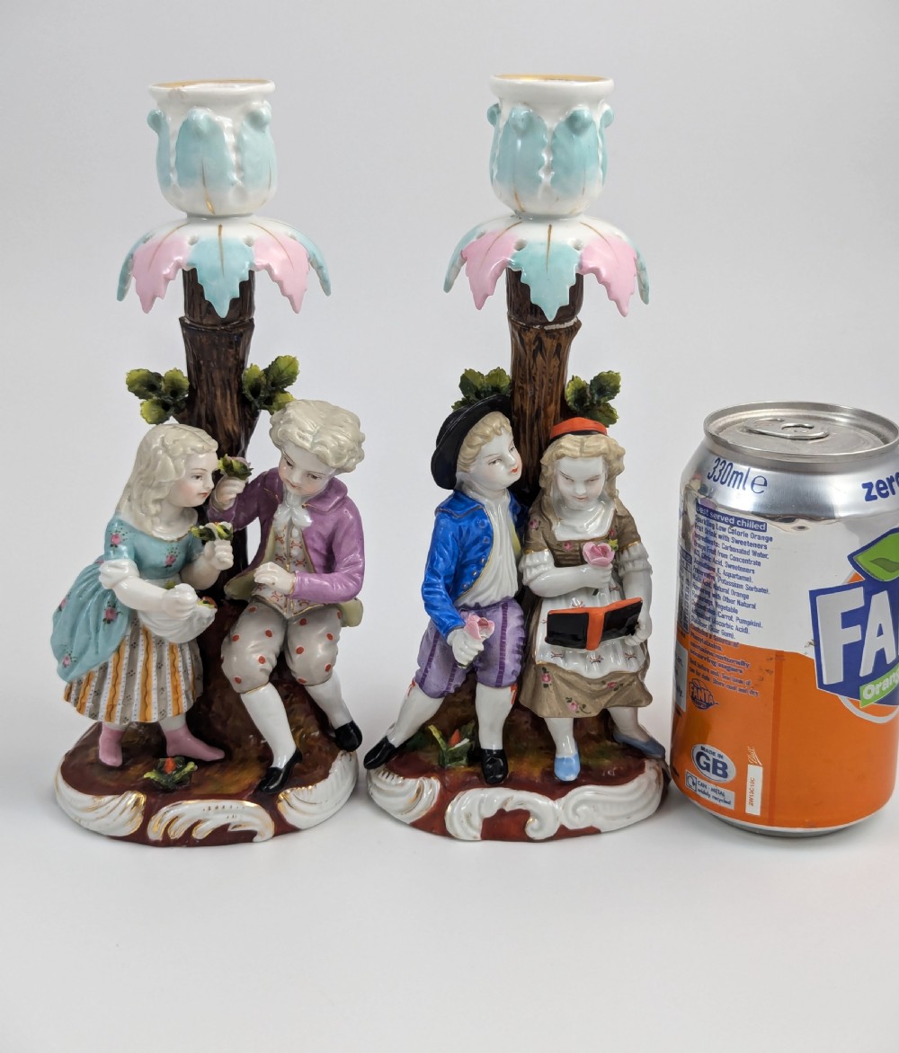 A pair of hand-painted porcelain figural candlesticks depicting eighteenth-century styled children beside floral tree columns. View VII