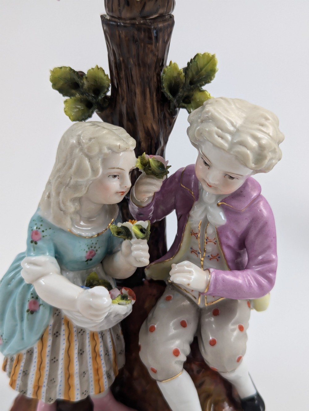 A pair of hand-painted porcelain figural candlesticks depicting eighteenth-century styled children beside floral tree columns. View VIII