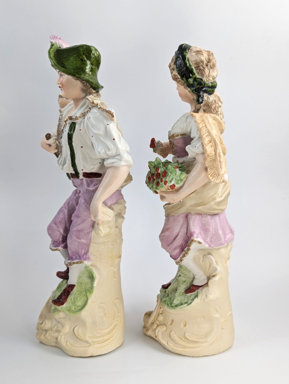 A pair of antique German bisque porcelain figurines depicting a man and woman in detailed pastoral attire with gilded accents on scroll bases. View II