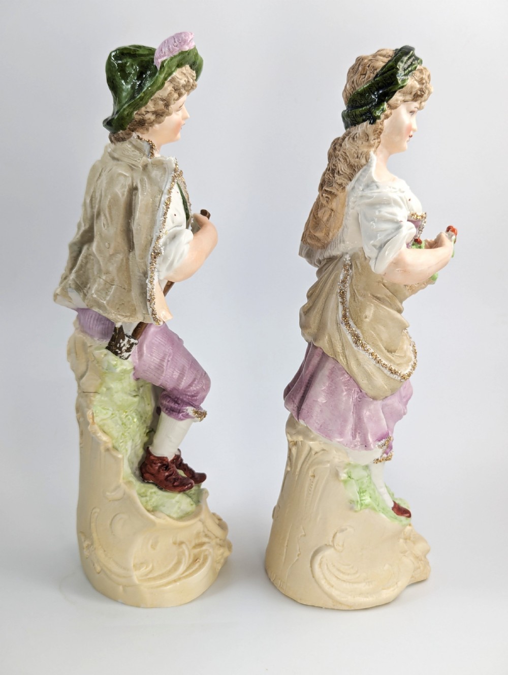 A pair of antique German bisque porcelain figurines depicting a man and woman in detailed pastoral attire with gilded accents on scroll bases. View IV