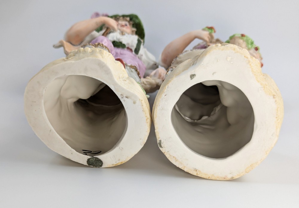 A pair of antique German bisque porcelain figurines depicting a man and woman in detailed pastoral attire with gilded accents on scroll bases. View V
