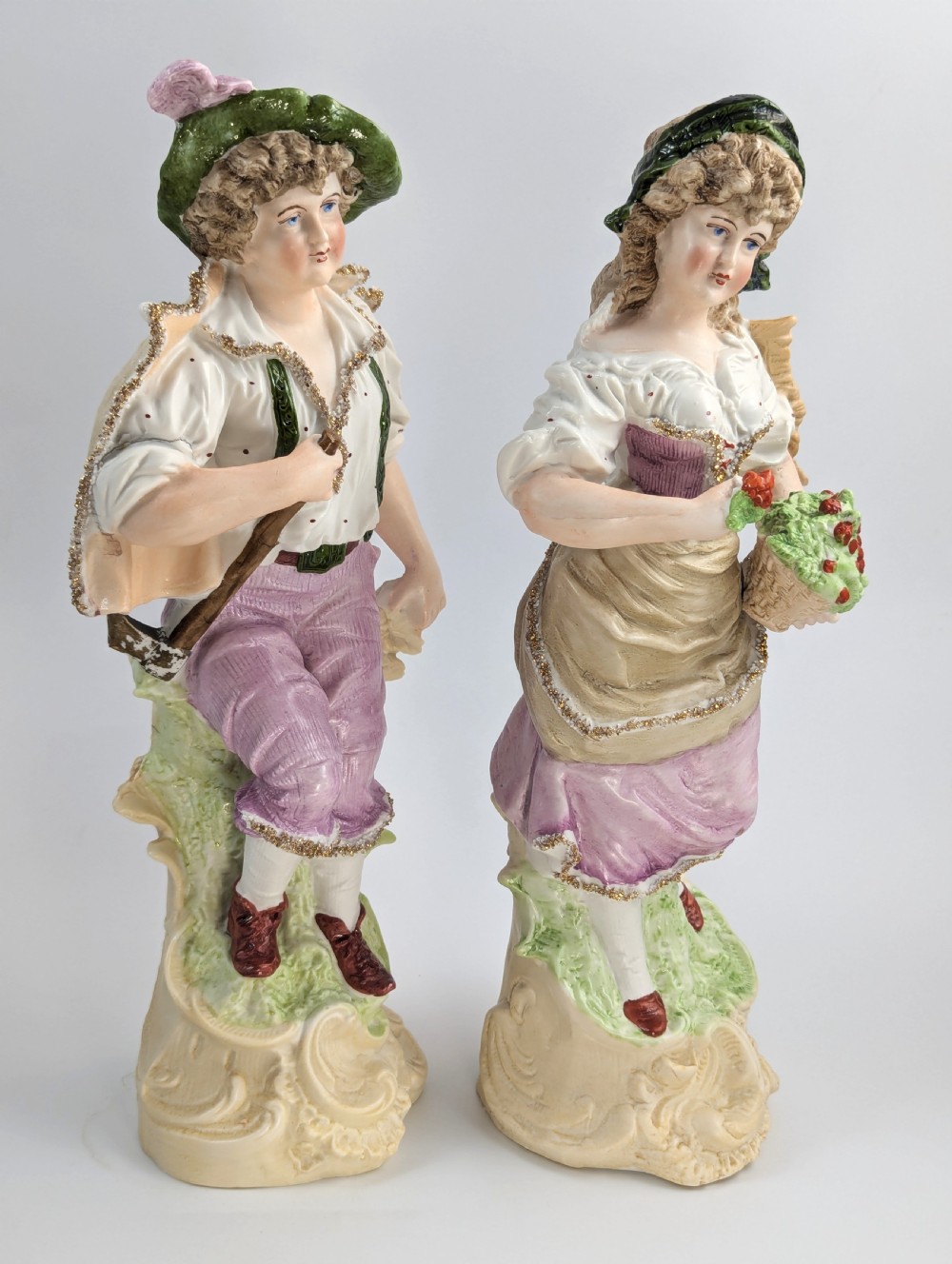 A pair of antique German bisque porcelain figurines depicting a man and woman in detailed pastoral attire with gilded accents on scroll bases. View VI