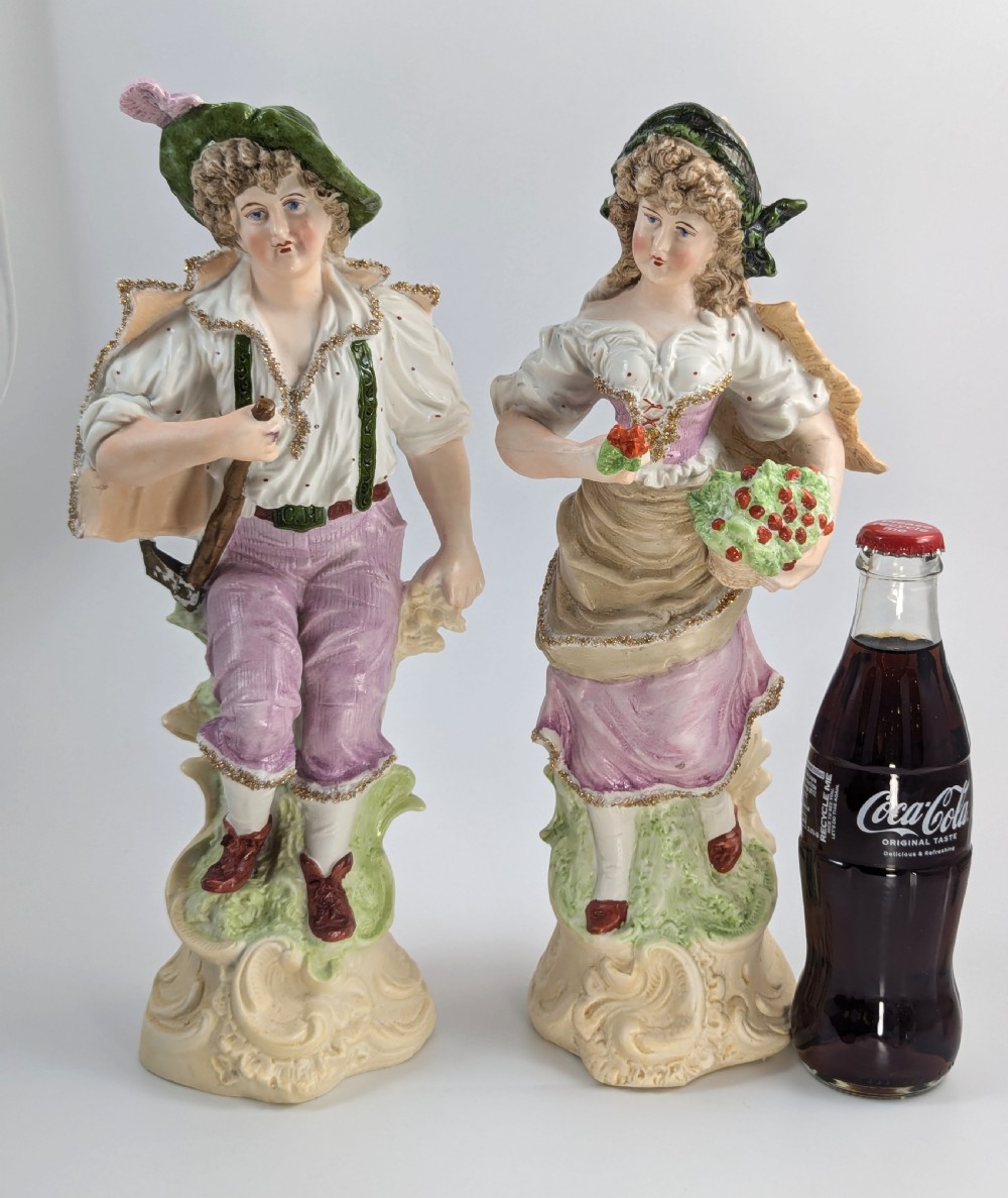 A pair of antique German bisque porcelain figurines depicting a man and woman in detailed pastoral attire with gilded accents on scroll bases. View VII