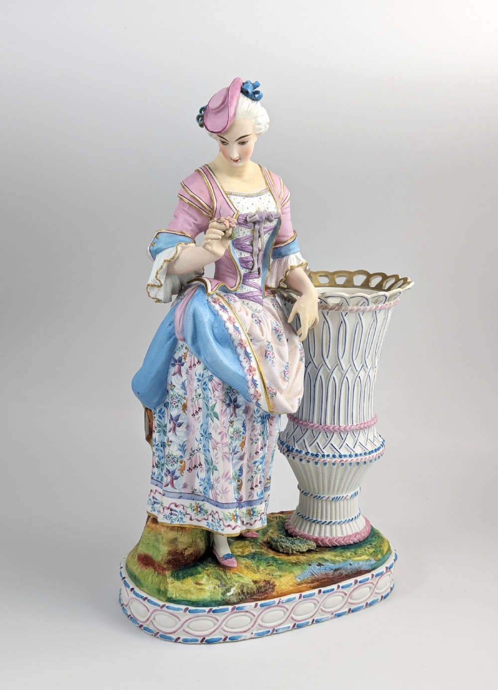 A 19th-century French bisque porcelain figural vase featuring a female figure in pastel Rococo costume standing beside a lattice-patterned vase on a painted base. View VIII