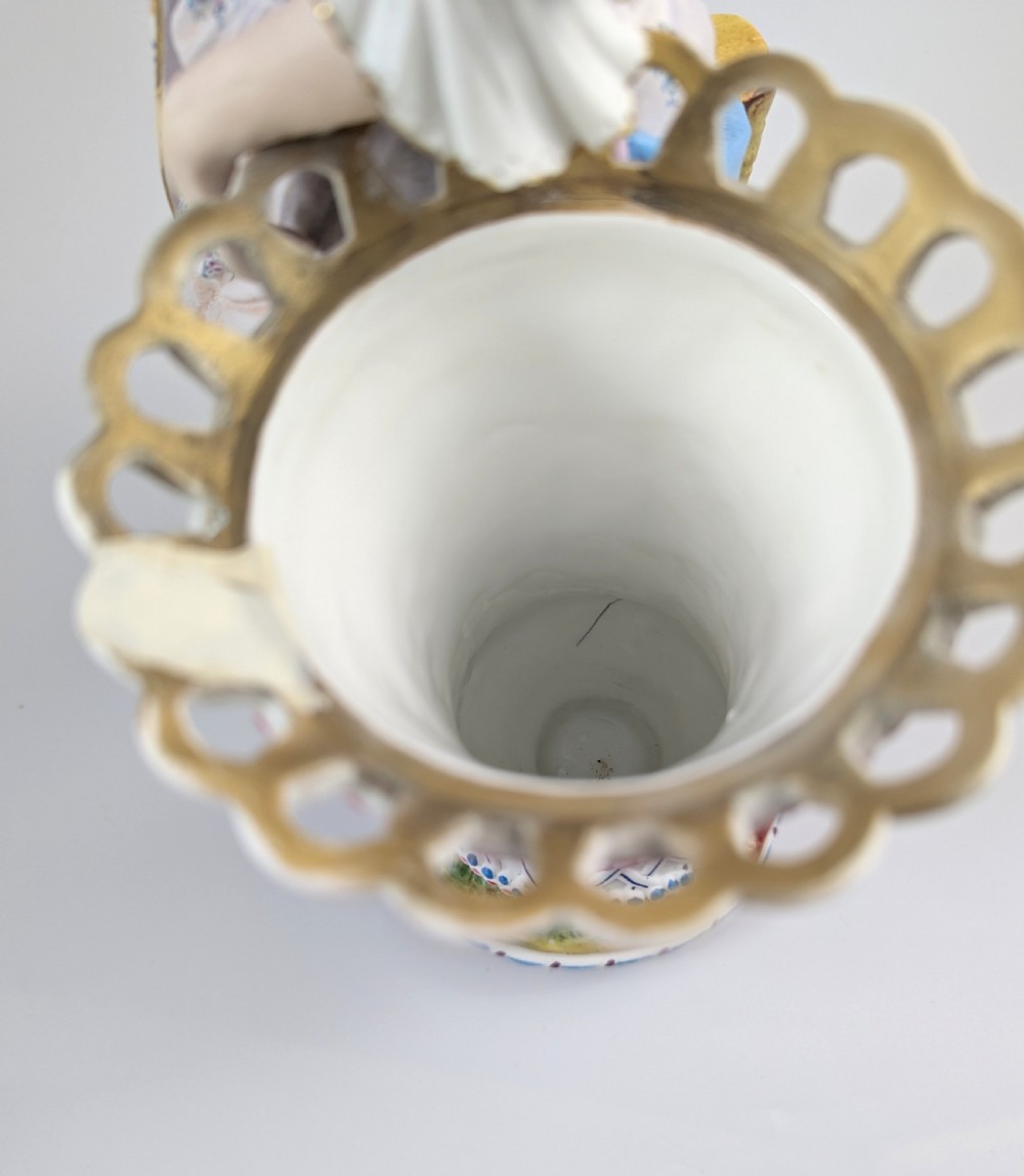 A 19th-century French bisque porcelain figural vase featuring a female figure in pastel Rococo costume standing beside a lattice-patterned vase on a painted base. View X