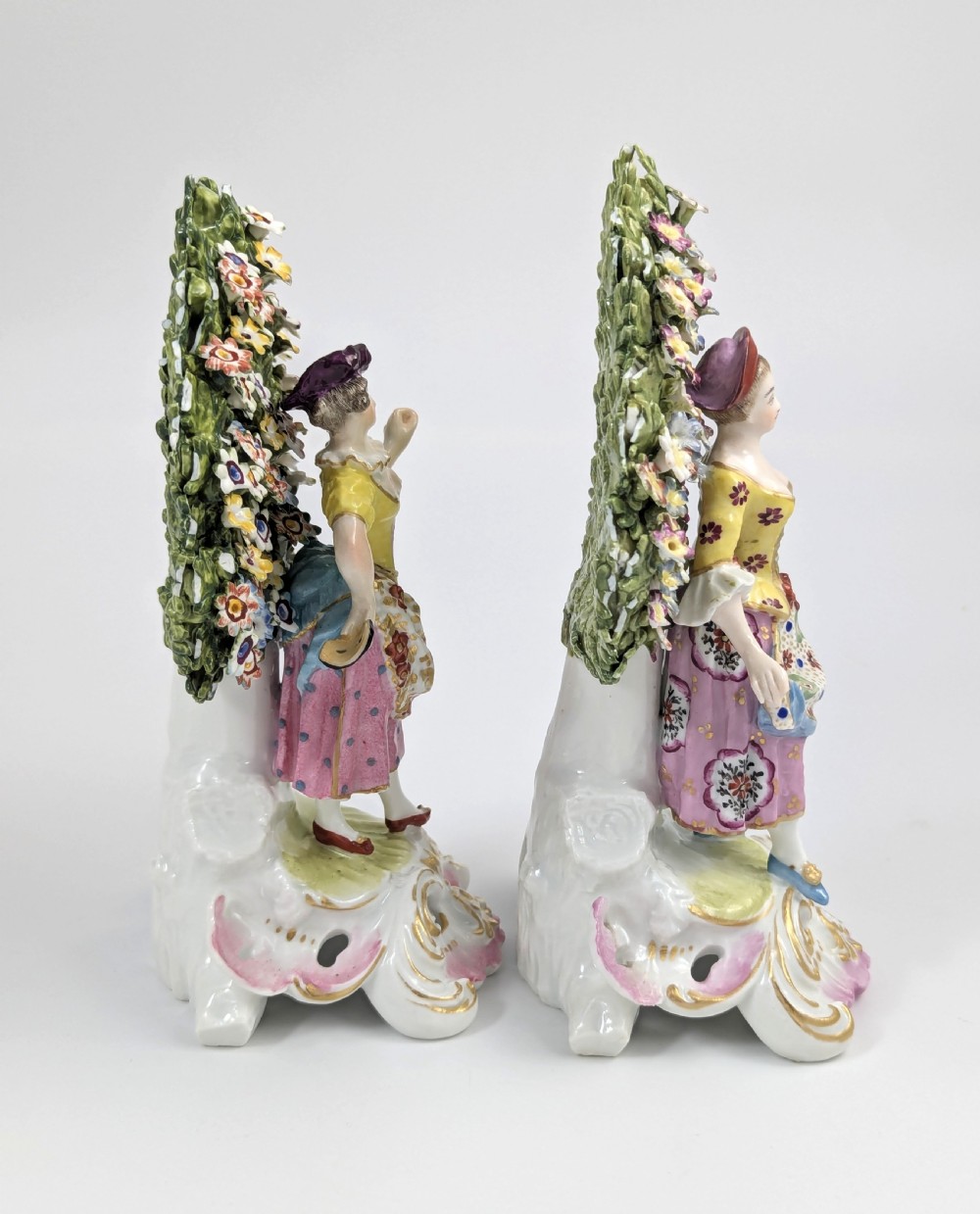 A pair of 19th-century Samson of Paris hand-painted porcelain figures standing against dense, flowering green bocage backgrounds on scrollwork bases. View IV
