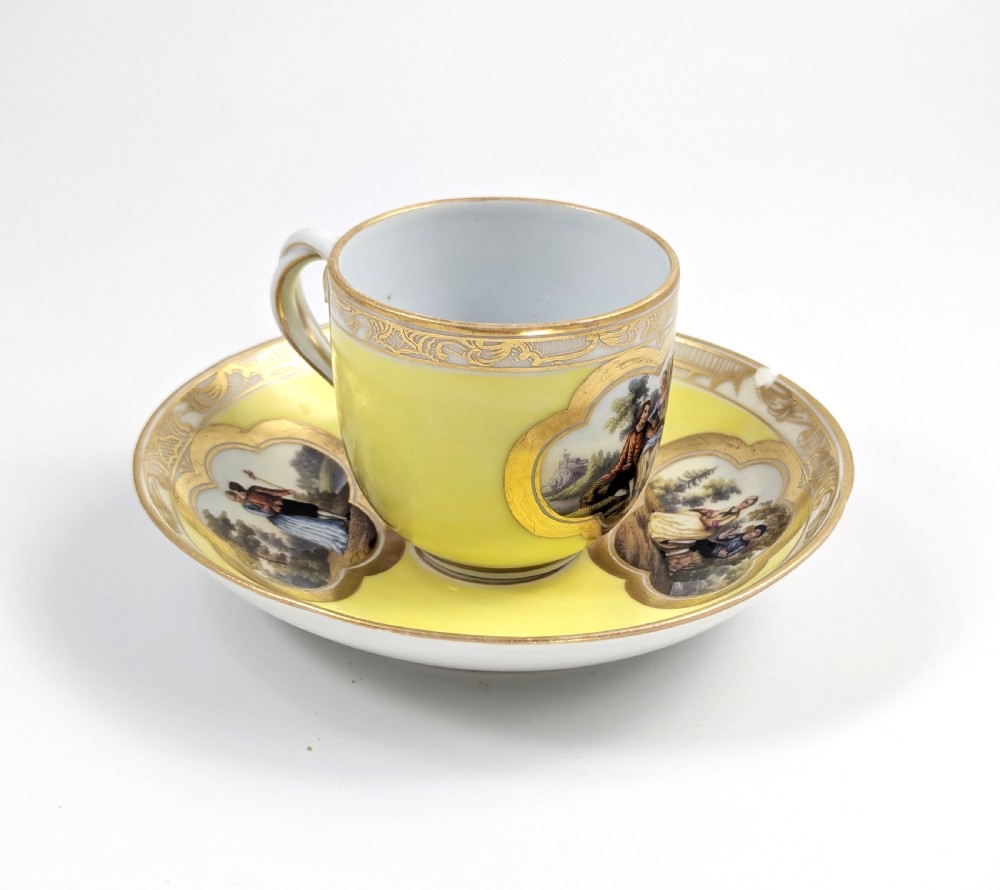 An antique nineteenth-century Meissen porcelain demitasse cup and saucer in yellow featuring hand-painted pastoral scenes set within intricate gilded cartouches. View III