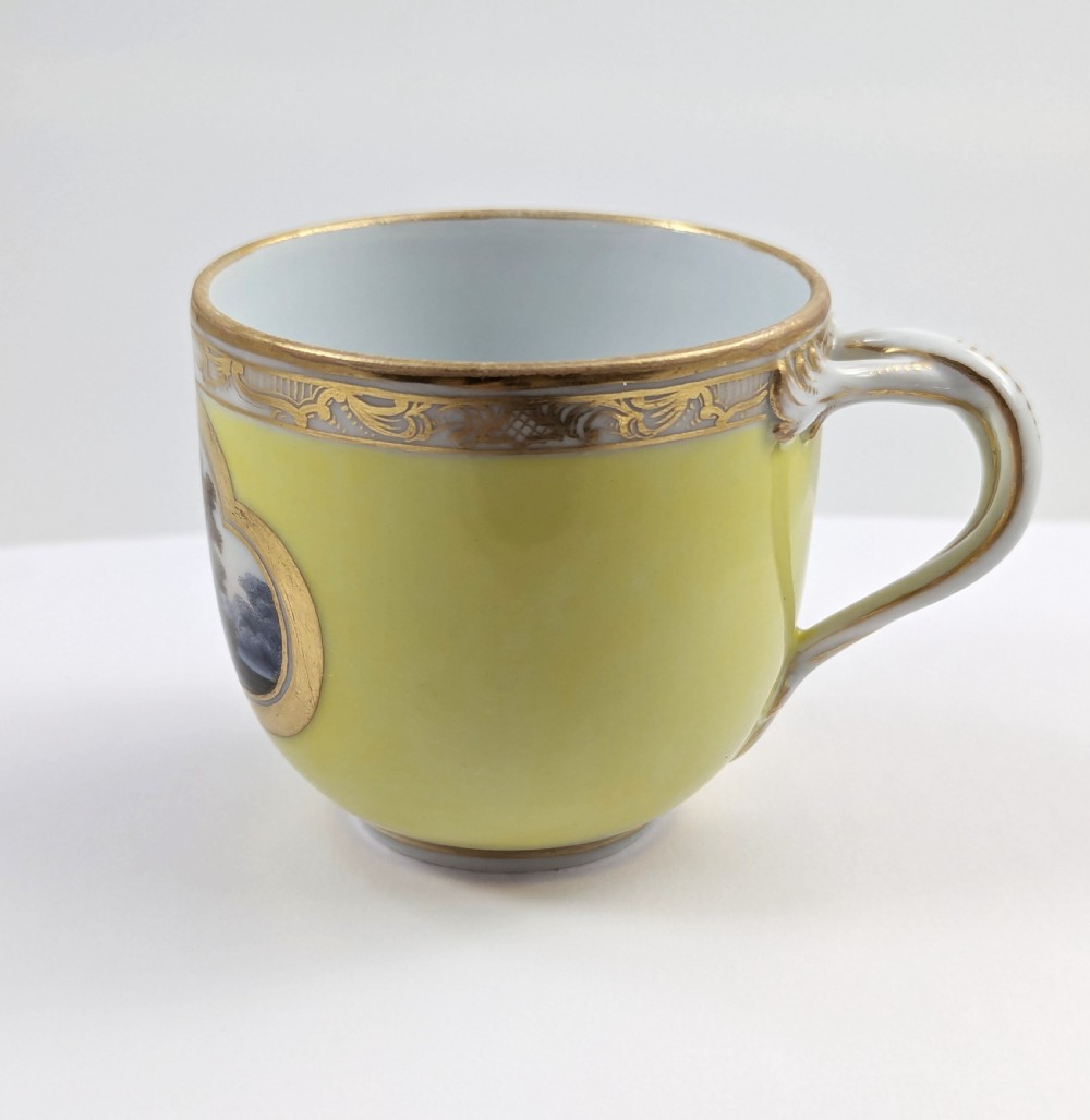 An antique nineteenth-century Meissen porcelain demitasse cup and saucer in yellow featuring hand-painted pastoral scenes set within intricate gilded cartouches. View IV